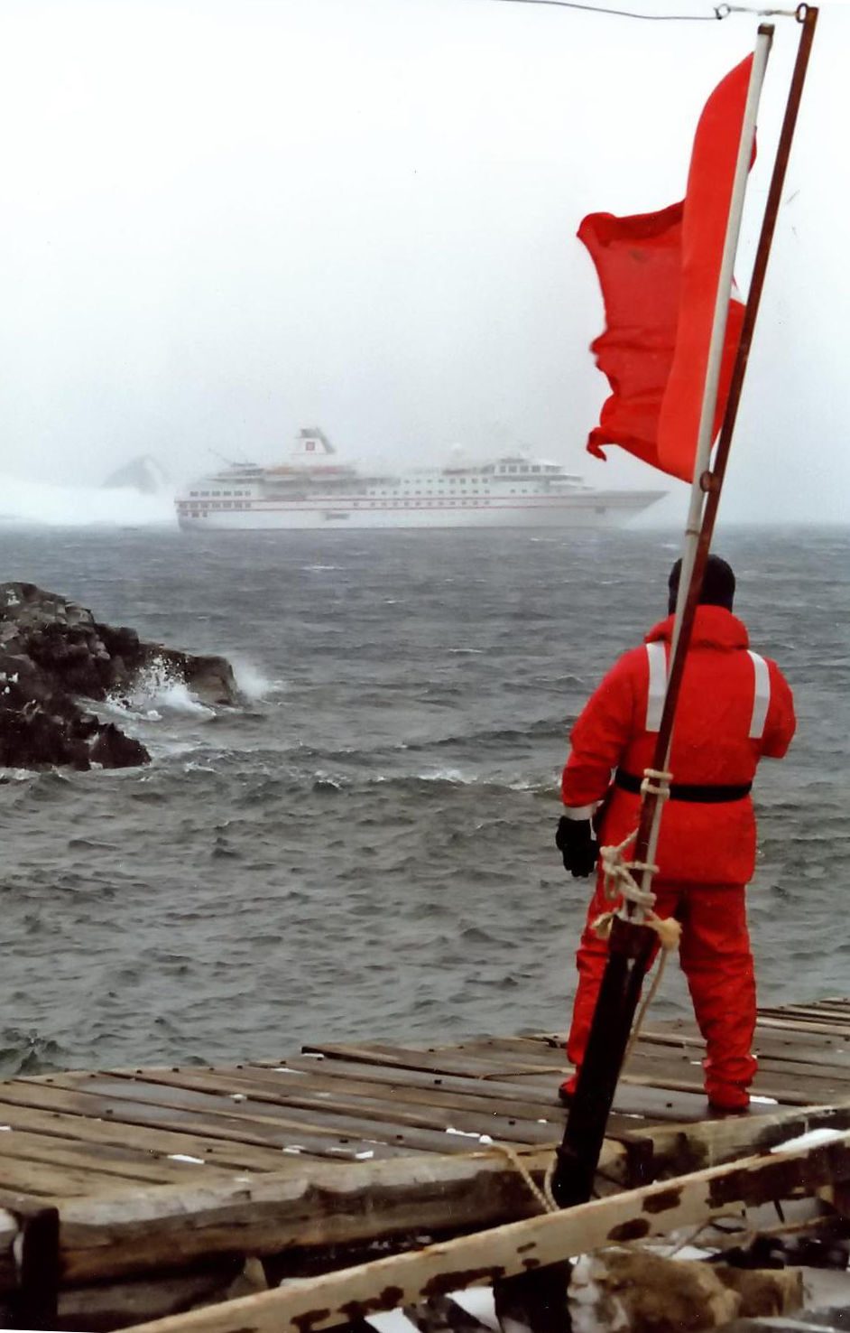 A red-hulled expedition cruise ship standing offshore in misty Antarctic weather