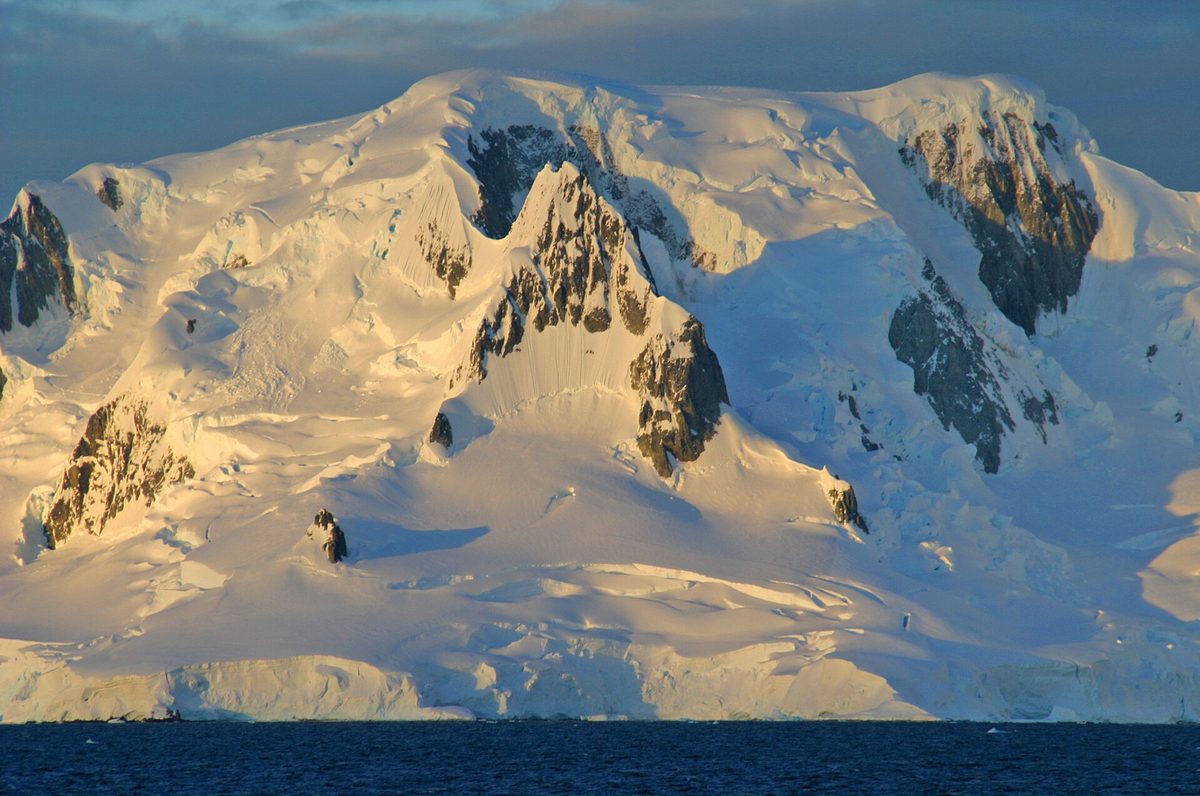 Snow-covered Antarctic peaks meeting the sea as a ship arrives